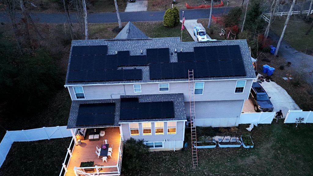 Aerial dusk view of a home with a full solar panel array on the roof and a deck lit below