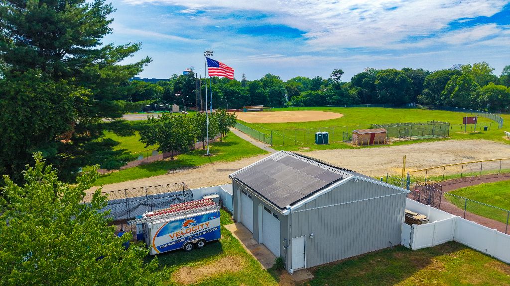 Velocity Energy branded equipment trailer parked at a community ballfield storage building job site